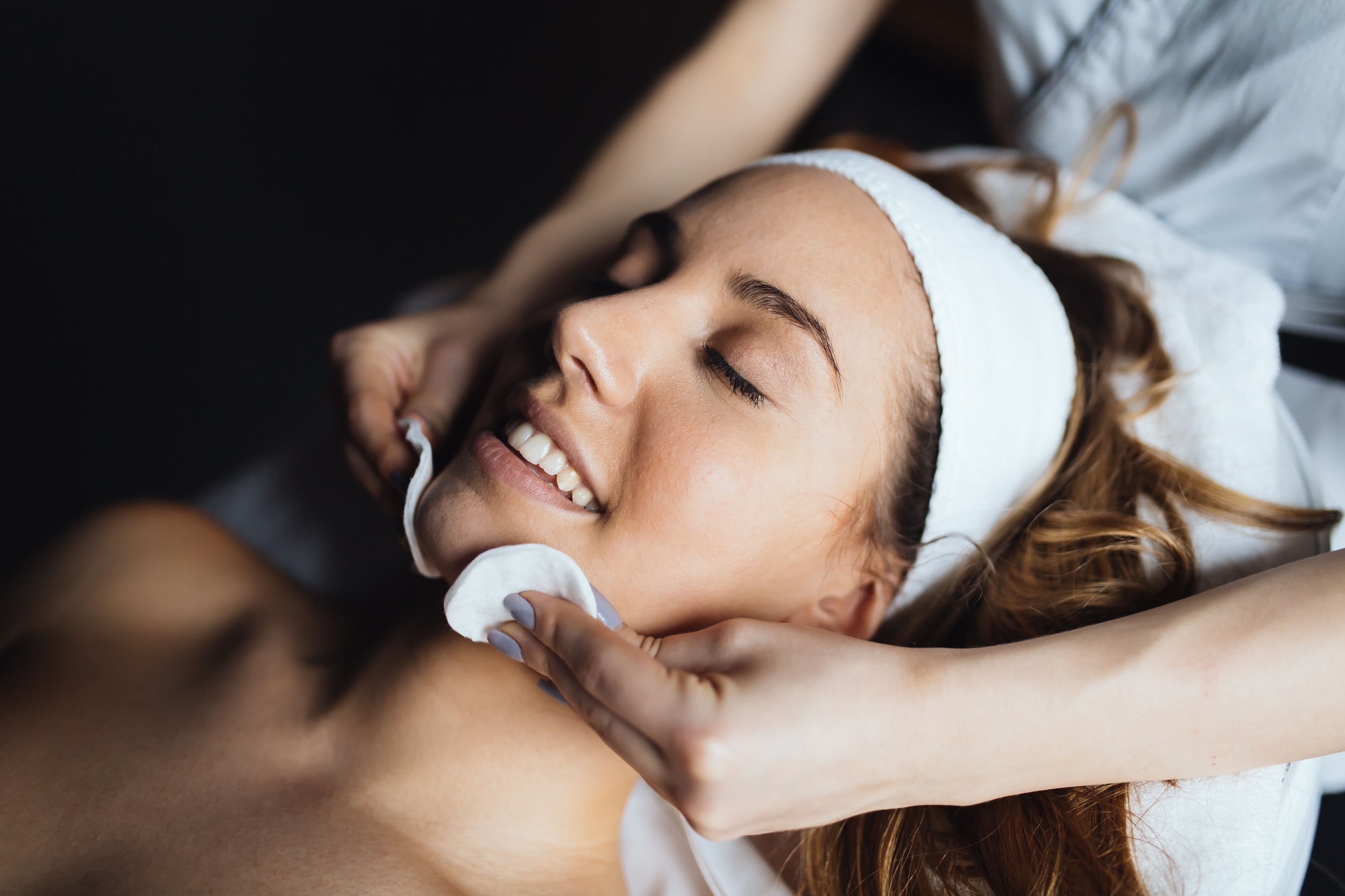 Woman smiling with eyes closed whilst receiving facial treatment
